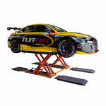 A race car featuring Tufflift branding is elevated on an orange EAE hydraulic scissor lift. The lift supports the car in a fully raised position. The car displays sponsor logos and a sleek black and yellow design.