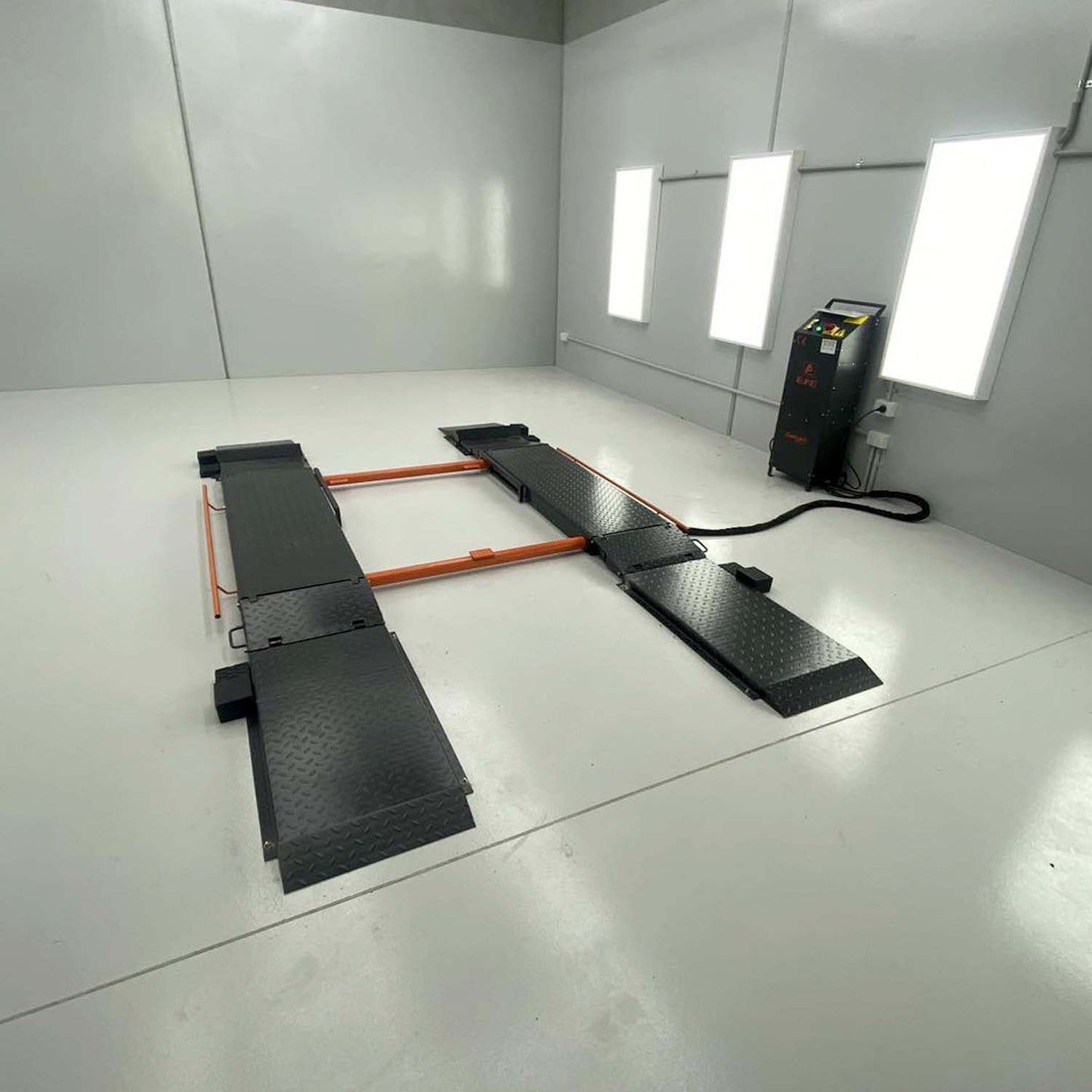An orange and grey EAE hydraulic scissor lift installed in a clean, white-walled workshop. The lift is in its fully lowered position with connected control units visible on the side.