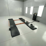An orange and grey EAE hydraulic scissor lift installed in a clean, white-walled workshop. The lift is in its fully lowered position with connected control units visible on the side.