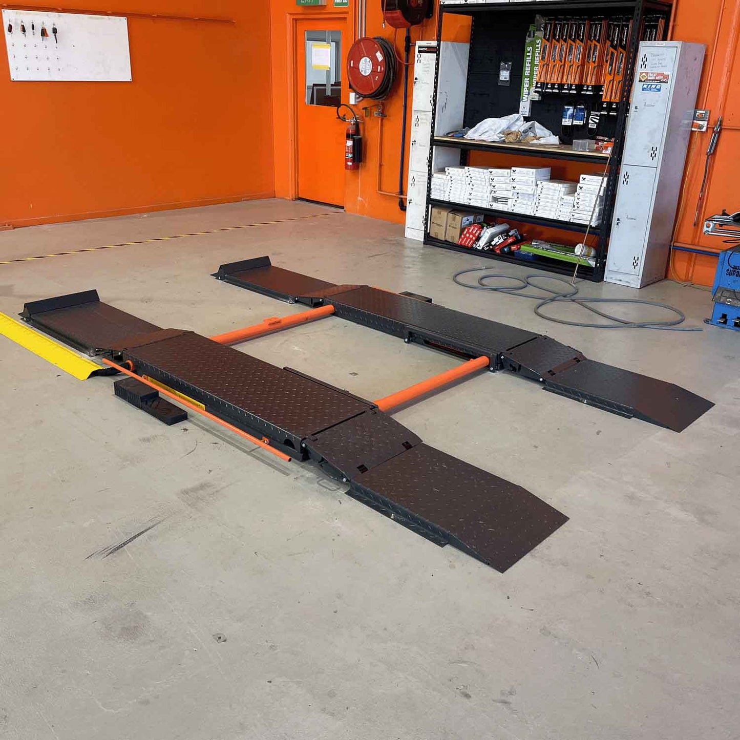 Scissor lift setup in a workshop environment, featuring orange and approach ramps designed to assist vehicles onto the lifting platform.