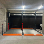 Empty platform 2 post car hoist system in a concrete-walled garage, featuring wide platforms with orange safety accents, ready for vehicle lifting. - 2 Post Parking Hoist - Full Platform Compact - 2.7 Ton | TL2.7HP
