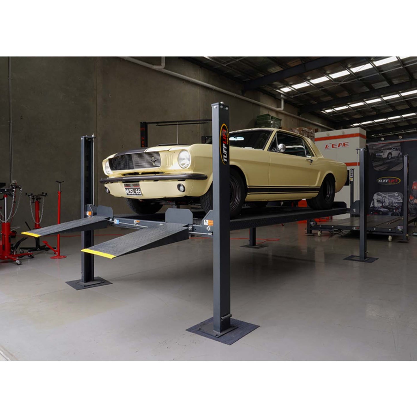 A classic yellow Mustang elevated on a charcoal grey four-post parking hoist in the Tufflift VIC warehouse showroom. - 4 Post Parking Hoist - High - 3.6 Ton | TL3.6PH-H