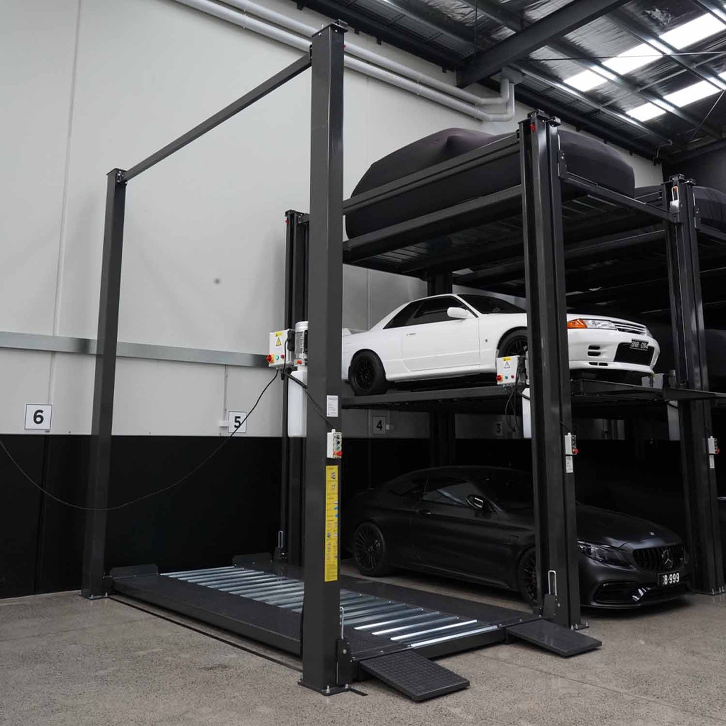 A robust four-post, three-tier parking lift with a durable dark grey frame, designed for maximizing vertical parking space and securely stacking vehicles across three levels. 4 Post Parking Hoist | Triple Stacker
