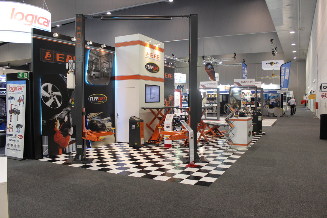 Tufflift exhibition stand at the Australian Auto Aftermarket Expo (AAAE) featuring car hoists and workshop scissor lifts on a checkered floor.