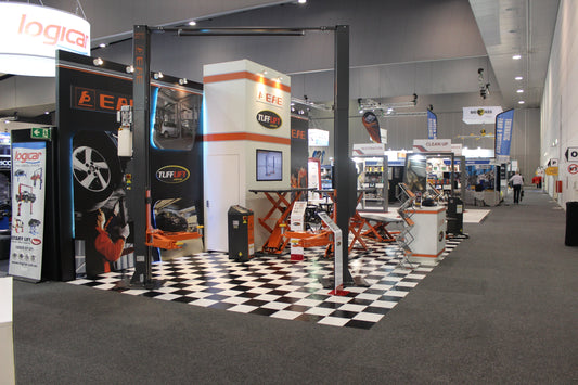 Tufflift exhibition stand at the Australian Auto Aftermarket Expo (AAAE) featuring car hoists and workshop scissor lifts on a checkered floor.