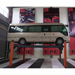 Minibus elevated on a four-post car hoist with orange columns inside a professional automotive workshop featuring EAE branding. - 4 Post Wheel Alignment Hoist - 4 Ton | EE-6435V2.B.48L.40T