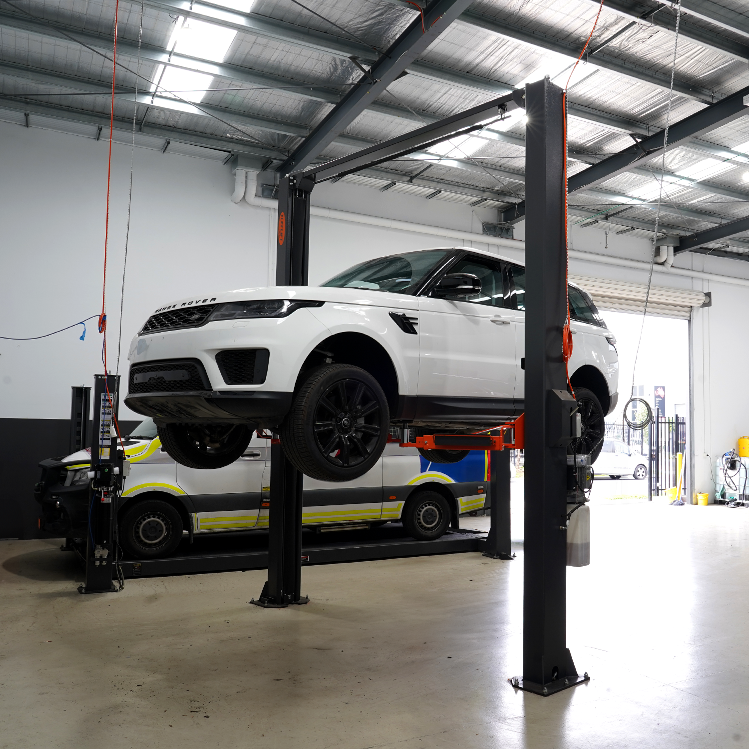 A white Range Rover lifted on a 2 post car hoist in an automotive workshop, showcasing the hoist's sturdy construction and lifting capability. - 2 Post Hoist Clear Floor - Extra High - 4.5 Ton | EE-C10-H