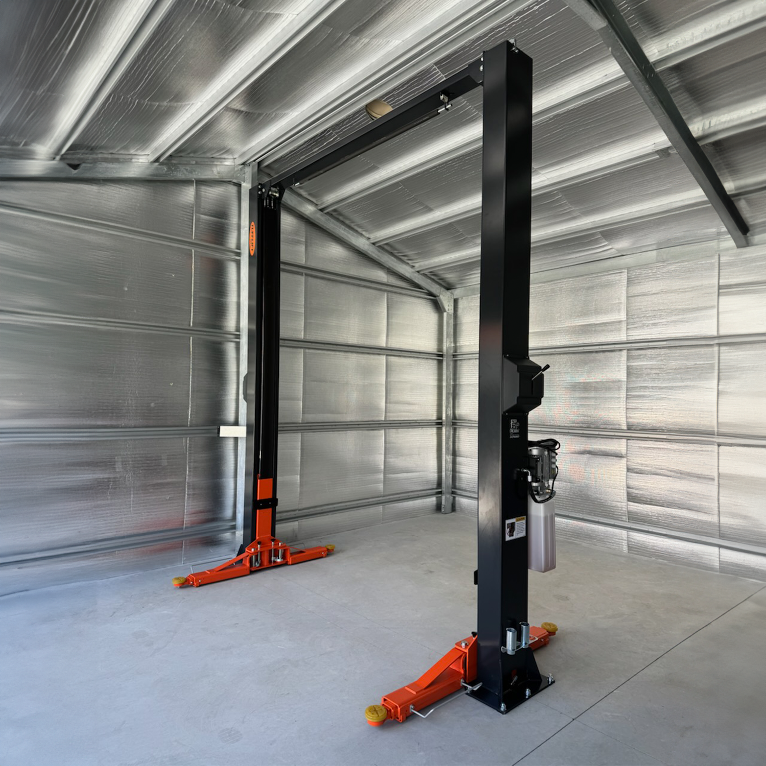 A two post car hoist with orange arms and a dark grey frame installed in a metallic, industrial-style shed with a concrete floor. - 2 Post Car Hoist - Low Profile Arms 85mm - Clear Floor - 4 Ton | EE-C9LPA