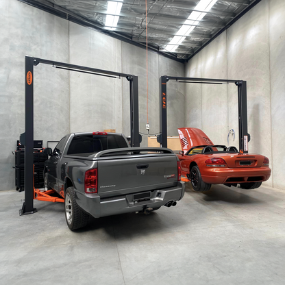 Workshop scene with two post car hoists in use: one holding a grey Dodge Ram truck and the other lifting an orange Dodge Viper with its hood open for maintenance. - 2 Post Car Hoist - Low Profile Arms 85mm - Clear Floor - 4 Ton | EE-C9LPA