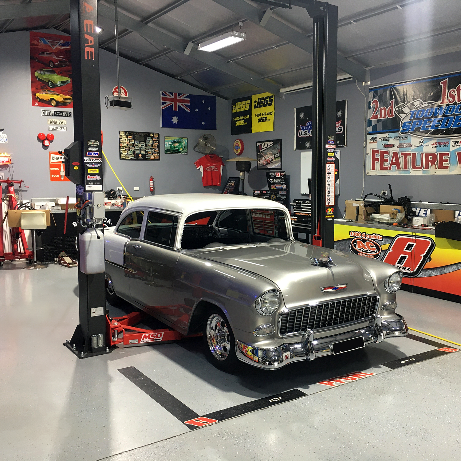 A classic car under a 2 post car hoist in a garage decked with automotive and racing decor. - 2 Post Clear Floor Hoist - 4 Ton | EE-C9