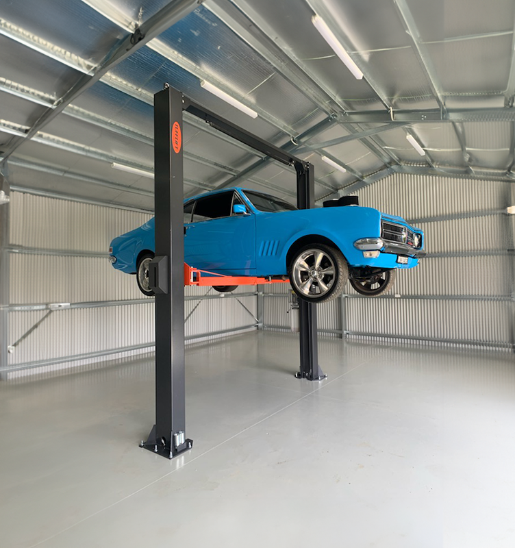Blue car on a two-post lift inside a metal garage.