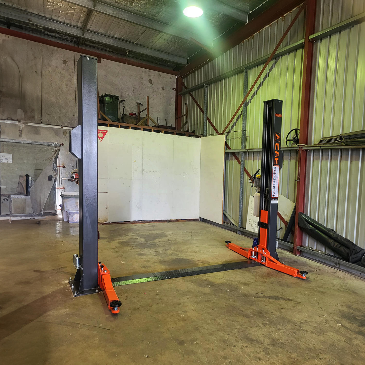 Tufflift 2 post baseplate car hoist set up in a corner of a rustic workshop with concrete flooring. - 2 Post Baseplate Hoist - 4 Ton | EE-F9