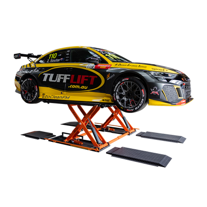 A race car featuring Tufflift branding is elevated on an orange EAE hydraulic scissor lift. The lift supports the car in a fully raised position. The car displays sponsor logos and a sleek black and yellow design.