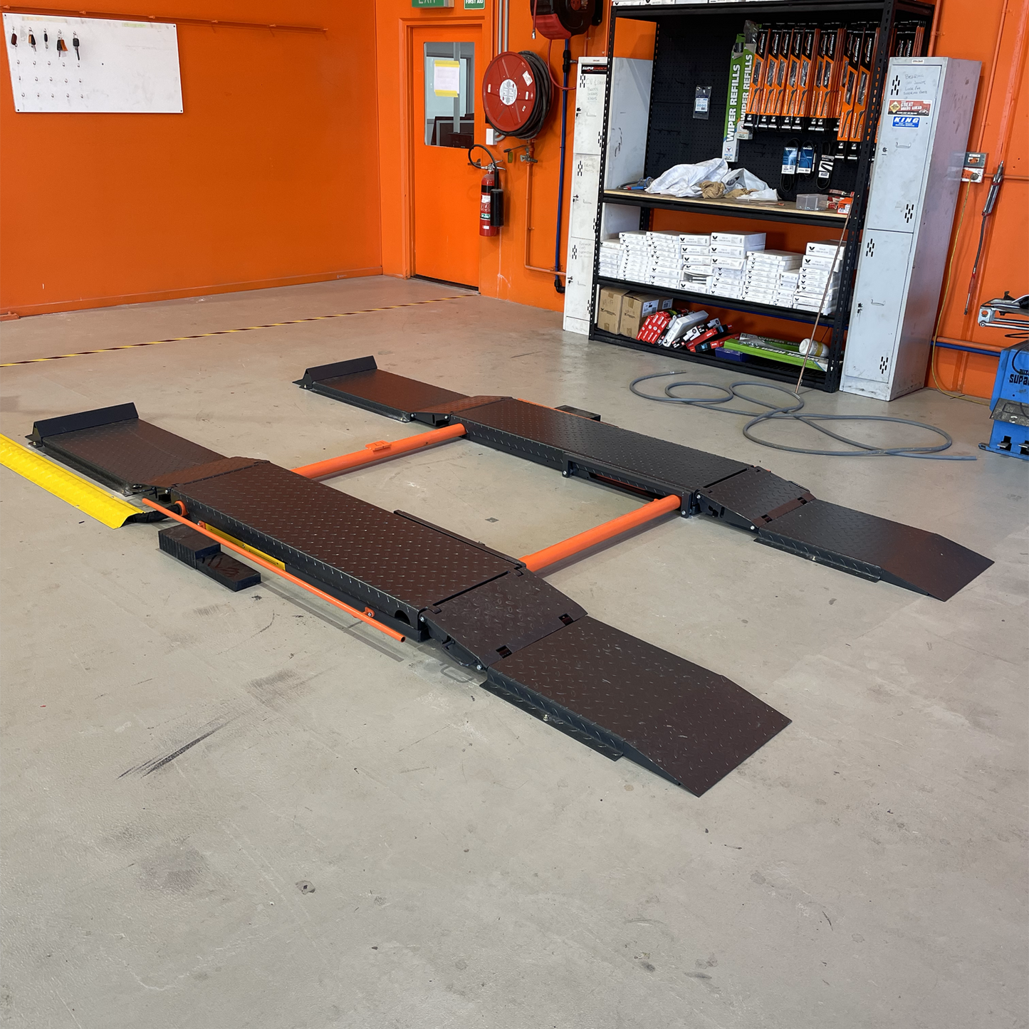 Scissor lift setup in a workshop environment, featuring orange and approach ramps designed to assist vehicles onto the lifting platform. 