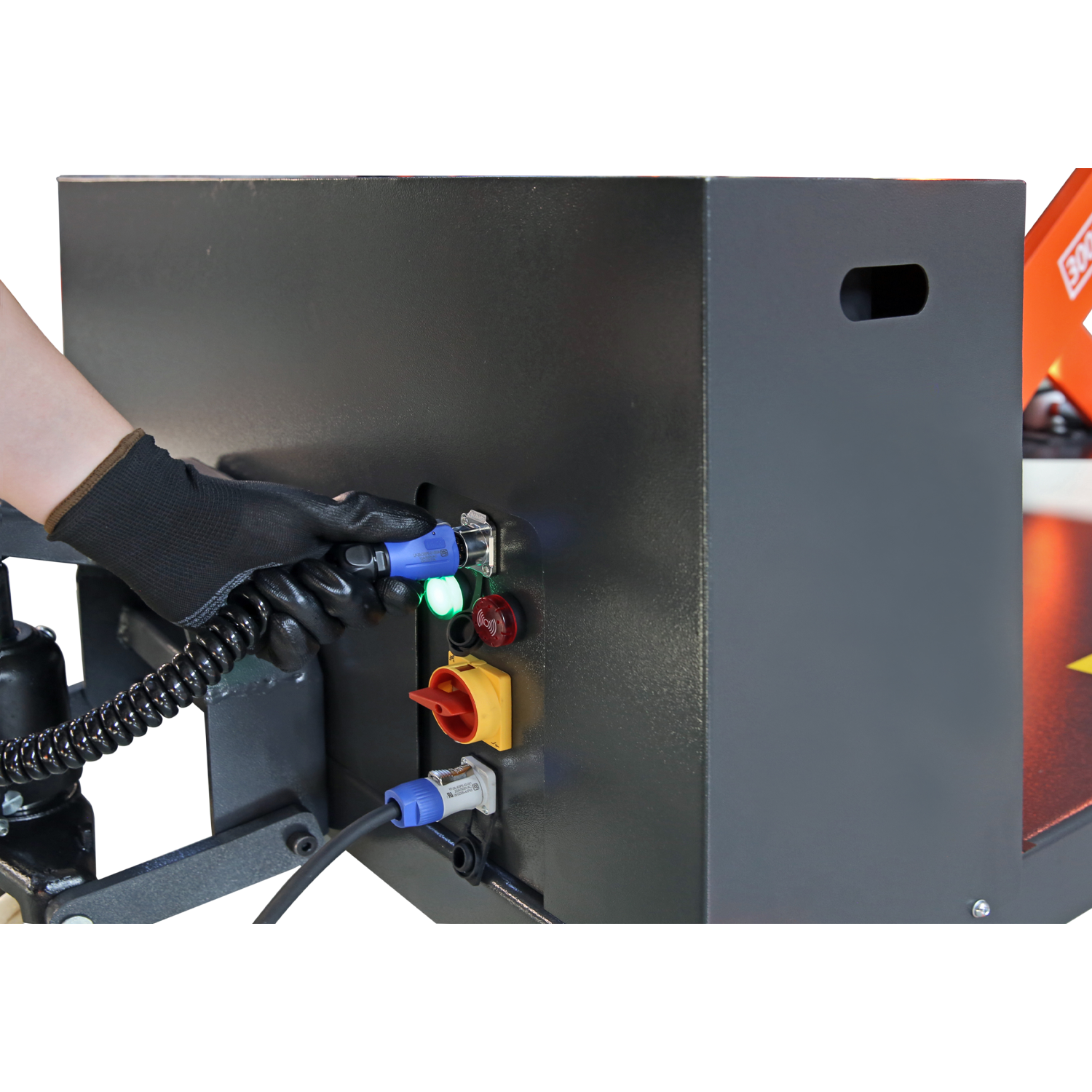 Gloved hand connecting a cable to a control panel on a lift, illustrating the setup and power connections for operating heavy-duty lifting equipment.