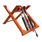 A close-up view of the hydraulic cylinders and mechanisms of an orange EAE scissor lift, model TS6600. The lift's support structure, labeled with a 2700kg capacity, is visible along with connected hydraulic lines and pistons.