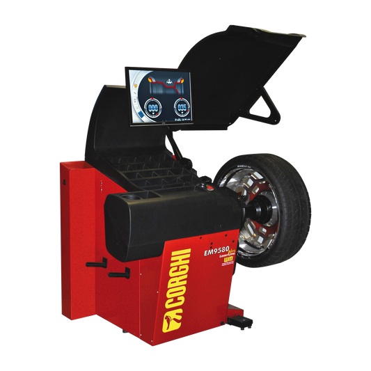 A red Corghi EM9580 Plus LaserLine wheel balancer with a mounted car tire. The machine features a digital display showing the wheel balancing process, with compartments for tools and accessories. The protective hood is raised, and the laser system is visible, designed for precise tire balancing.