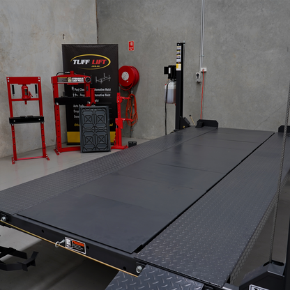 Infill kit installed on a 4 post car hoist platform lift, creating a continuous, level surface with diamond-plate steel edges and smooth center panels. The setup is situated in a workshop with Tuff Lift branding and other automotive equipment visible in the background.