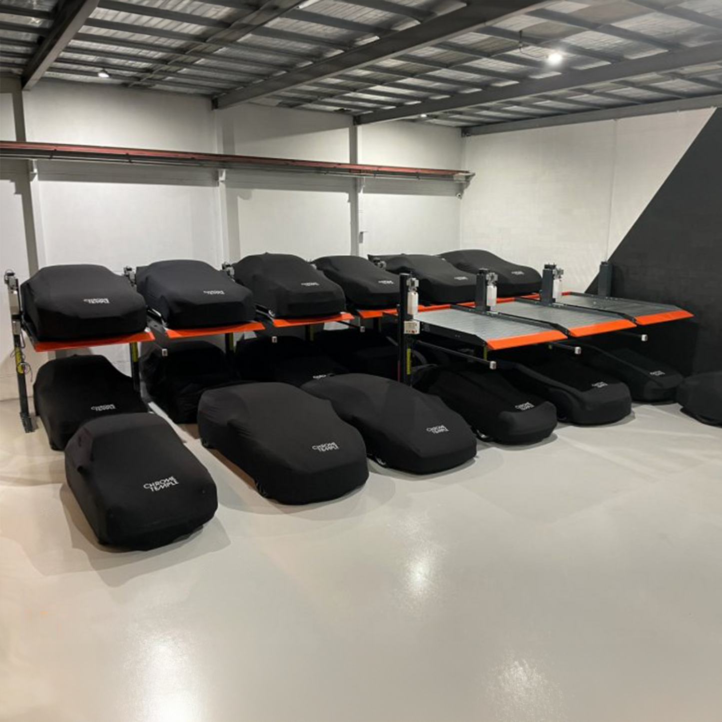 Indoor storage facility featuring a 2 post parking car hoist system, with multiple cars covered in black protective covers both on the ground and elevated platforms. - 2 Post Parking Hoist - Full Platform Compact - 2.7 Ton | TL2.7HP