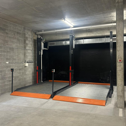 Two platform 2 post car hoist system installed in a concrete-walled garage, featuring wide platforms with orange safety accents, designed for efficient vehicle lifting and servicing. - 2 Post Parking Hoist - Full Platform Compact - 2.7 Ton | TL2.7HP