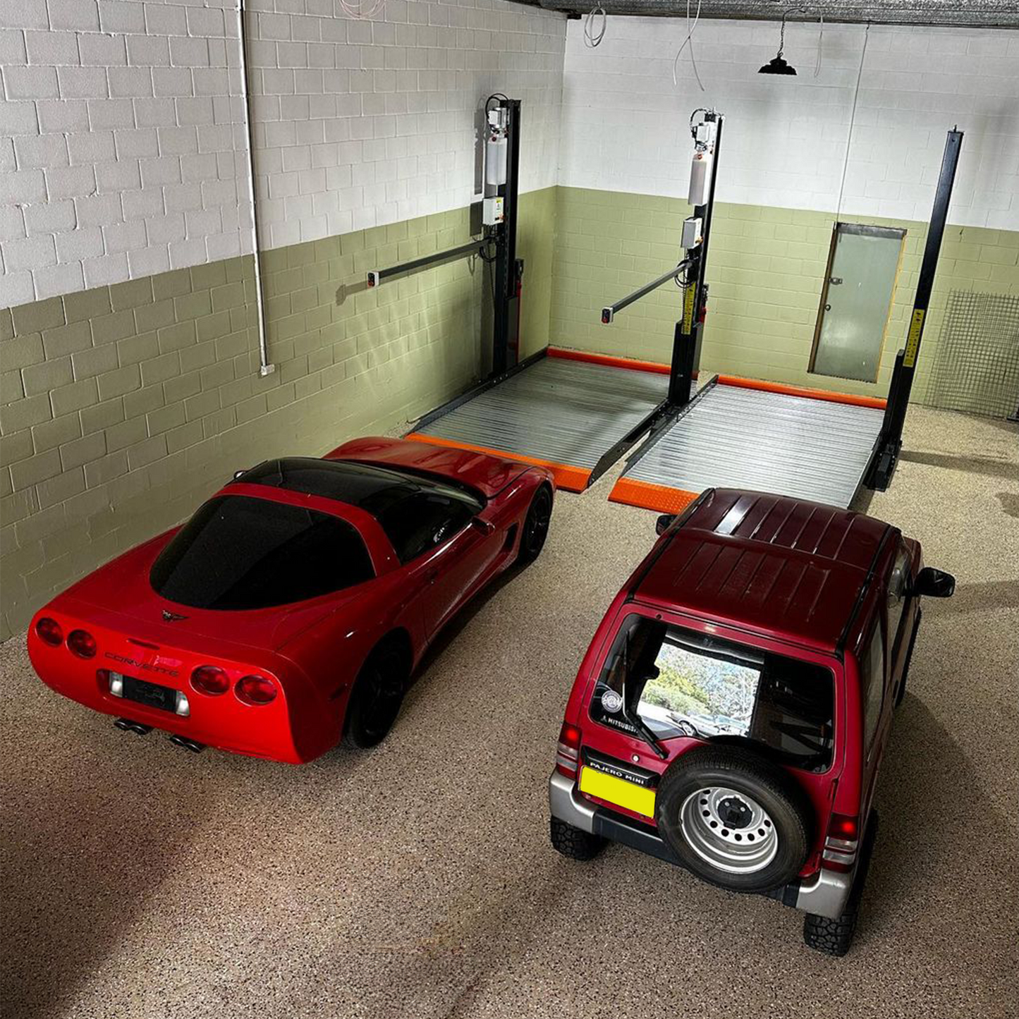 Concrete warehouse with two 2 post car hoists, featuring wide platforms with orange safety accents, and two vehicles, a red sports car and a red SUV, parked nearby." - 2 Post Parking Hoist - Full Platform Compact - 2.7 Ton | TL2.7HP