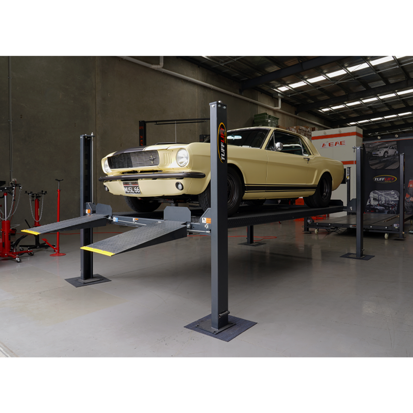 A classic yellow Mustang elevated on a charcoal grey four-post parking hoist in the Tufflift VIC warehouse showroom. - 4 Post Parking Hoist - High - 3.6 Ton | TL3.6PH-H