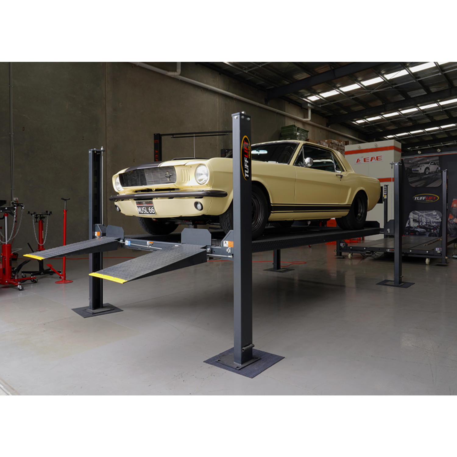 A classic yellow Mustang elevated on a charcoal grey four-post parking hoist in the Tufflift VIC warehouse showroom. - 4 Post Parking Hoist - High - 3.6 Ton | TL3.6PH-H