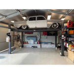 A vintage car is elevated on a 4 post parking hoist inside a well-organized garage, showcasing storage efficiency and a workspace for automotive maintenance.
