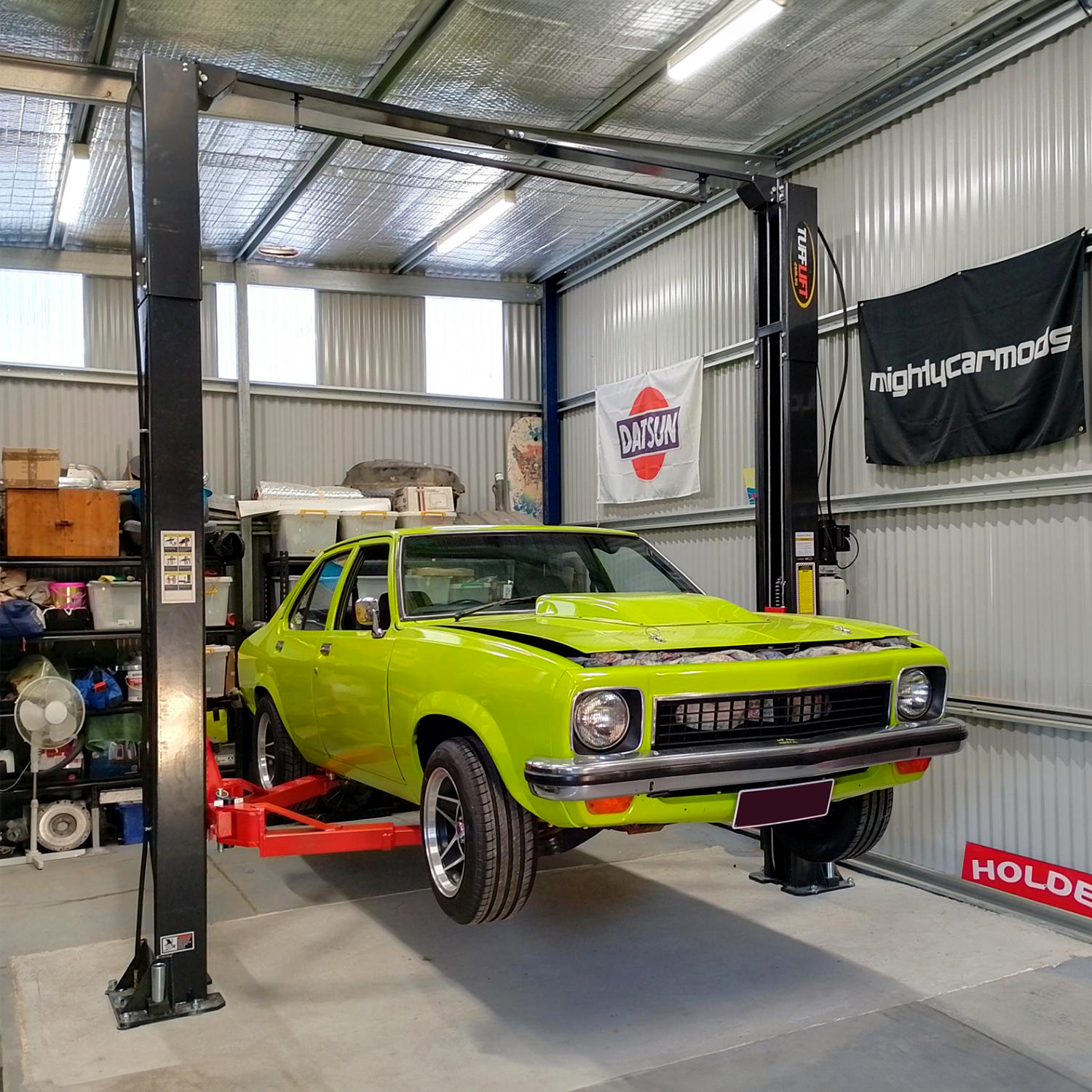 A bright lime green vintage car is elevated on a car lift in a well-organized garage. Shelves in the background hold various tools and equipment, with banners hanging on the walls. - 2 Post Clear Floor Hoist - 4 Ton | TL4.0OHDI