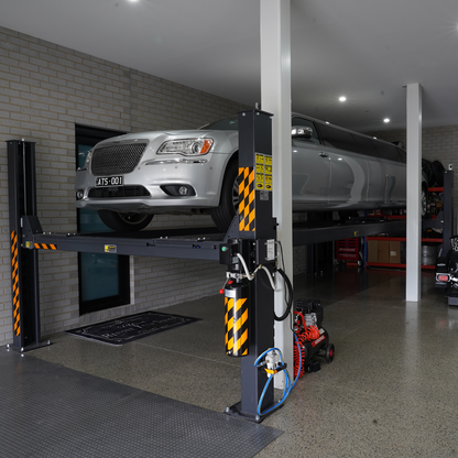 A long silver limousine elevated on a 7-meter 4 post hoist inside a modern garage with industrial-style flooring and walls