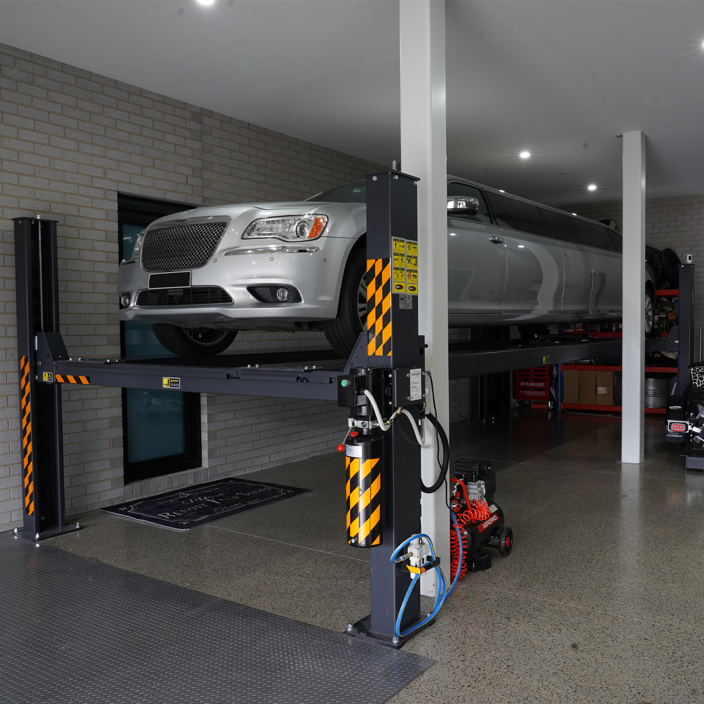 A long silver limousine elevated on a 7-meter 4 post hoist inside a modern garage with industrial-style flooring and walls