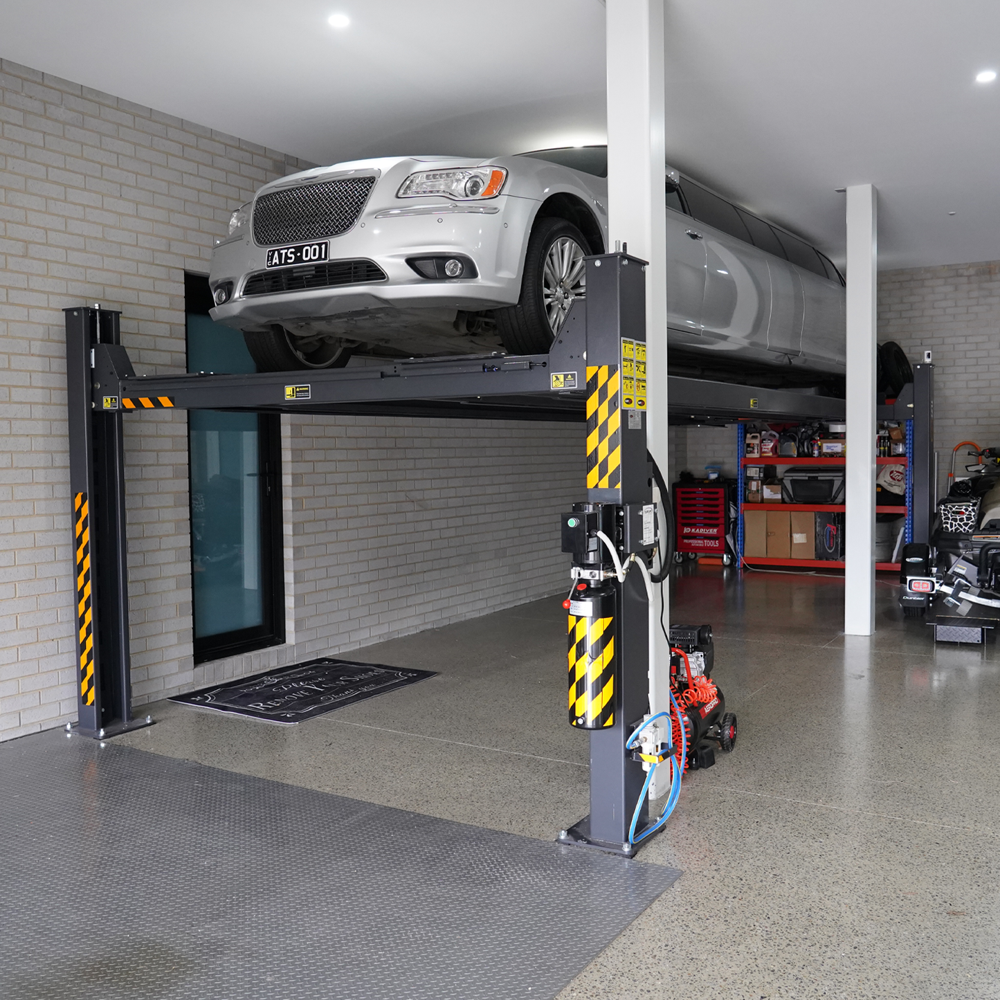 A silver limousine lifted on a 7-meter 4 post hoist inside a garage, with a polished concrete floor, tools, and equipment visible in the background.