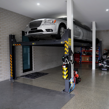 A silver limousine lifted on a 7-meter 4 post hoist inside a garage, with a polished concrete floor, tools, and equipment visible in the background.