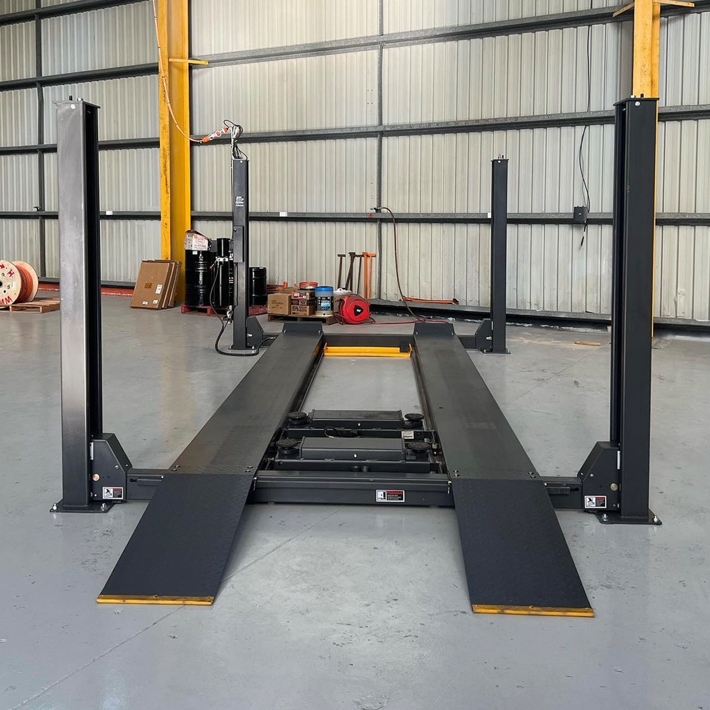 Front view of a four-post car hoist with drive-on ramps installed in a spacious industrial garage, ready for vehicle maintenance and servicing. - 4 Post Workshop Hoist - 6 Ton | TL6.0PH