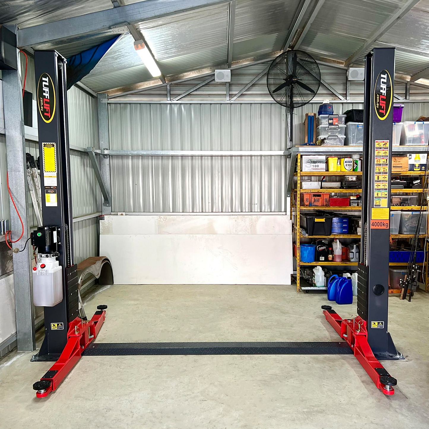 A clean and organized garage featuring a Tufflift 2 post baseplate car hoist with bright red arms. - 2 Post Baseplate Hoist - 4 Ton | TLD4.0BP