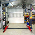 A clean and organized garage featuring a Tufflift 2 post baseplate car hoist with bright red arms. - 2 Post Baseplate Hoist - 4 Ton | TLD4.0BP