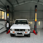 A classic white car parked between the posts of a Tufflift 2 post car hoist - 2 Post Baseplate Hoist - 4 Ton | TLD4.0BP