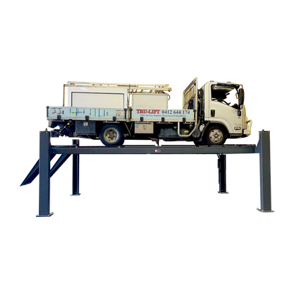 A heavy truck elevated on a four-post, eight ton workshop car hoist in a workshop setting. - 4 Post Wheel Alignment Hoist - 8.0 Ton | TLD8.0WA